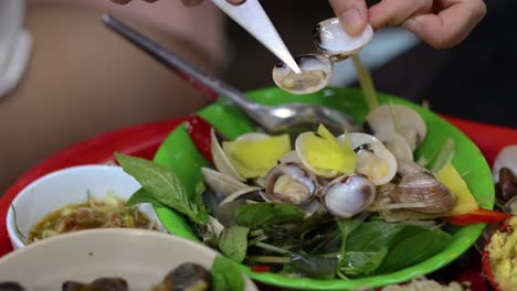 hands shucking clams with knives over a bowl