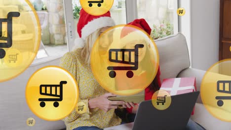 animación de iconos de carretillas de compras en línea sobre madre y hija caucásicas en navidad