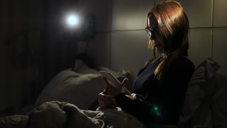 Adult woman reads an e-reader device in a dark bedroom