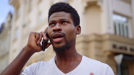 anxious man talking mobile in city. afro guy having phone conversation on street