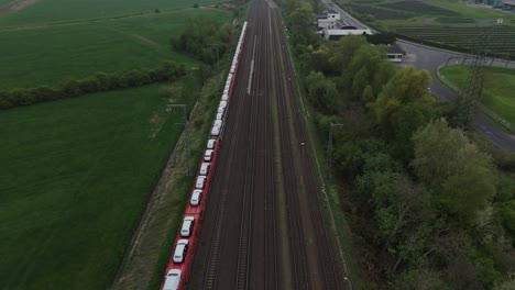 aerial shot of railway tracks near leer, germany, on a cloudy afternoon. cargo train with white vehicles on red flatcars. wide landscape view with green fields and industrial surroundings. shot in 4k.