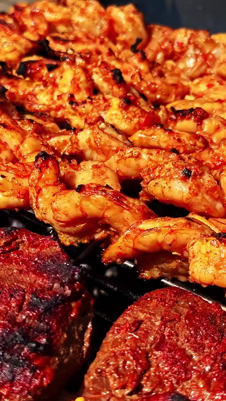 Primo piano estremo di gamberi marinati piccanti e spiedini di maiale carbonizzati che sfrigolano su una griglia esterna in un mercato di strada lettone