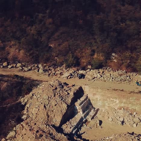people are walking near sand quarry with the stones below. view of the quarry with the forest. camera motion up