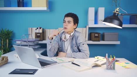 Clever-young-male-student-thoughtfully-picks-up-his-glasses-while-looking-at-laptop-and-looking-thoughtfully-at-the-screen.