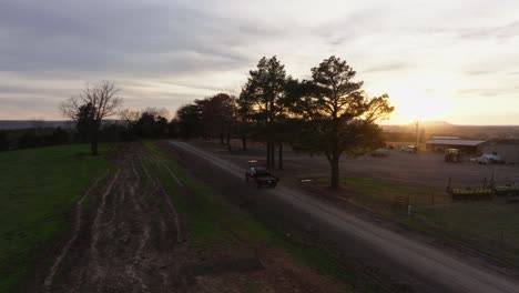 truck driving alone on a dirt road surrounded by trees and a farm in the sunset during a late afternoon