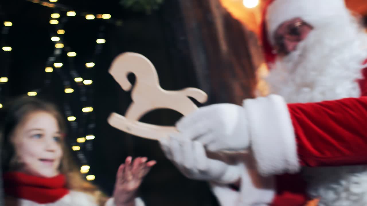 Santa Claus gives a little girl a Christmas toy a horse
