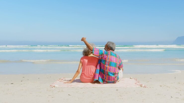 Rear view of active senior African American couple relaxing on blanket in the sunshine at beach 4k