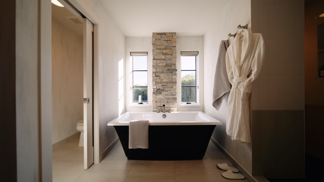 A modern bathroom with a freestanding tub, stone accent wall, large windows, and soft lighting, creating a serene and relaxing atmosphere