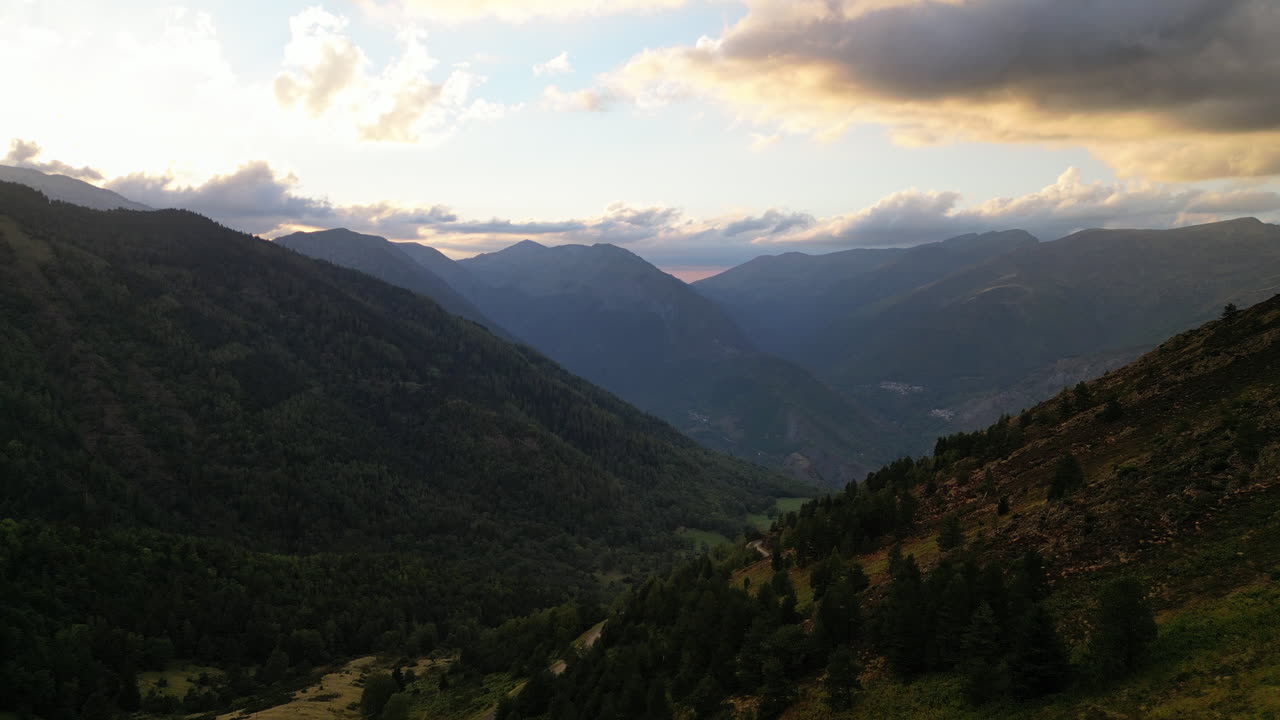 RIPRESA DRONE su una valle tra le montagne con il tramonto sullo sfondo, alberi a terra e nuvole arancioni