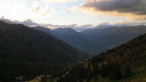 drone shot over a valley in the mountains with sunset behind, trees on the ground and orange clouds