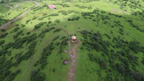 Drone-shot-of-Hindu-temple-at-the-edge-of-the-mountain-surrounded-by-lush-greenery,-Trimbakeshwar,-Nashik,-India