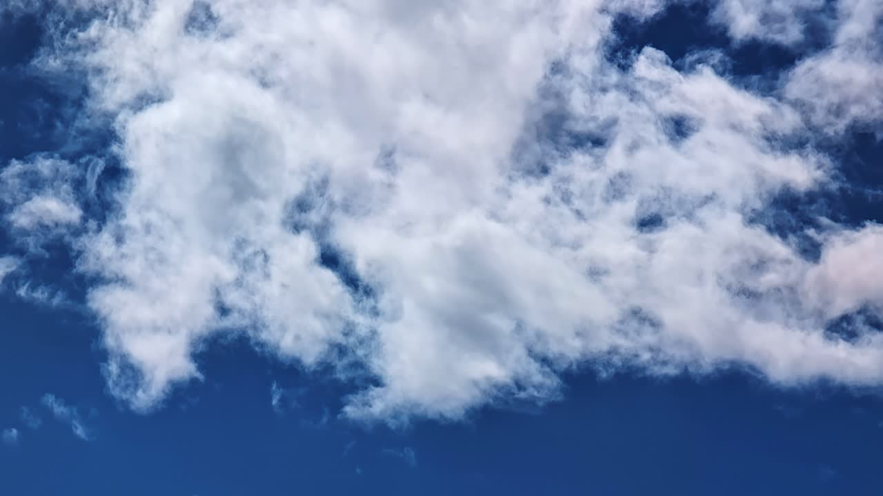 Fluffy white clouds drifting across deep blue sky on bright clear summer day. Natural background