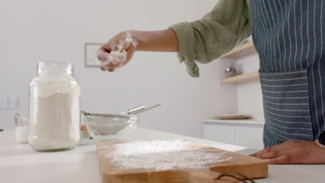 African-American-young-woman-is-sprinkling-flour-on-wooden-board