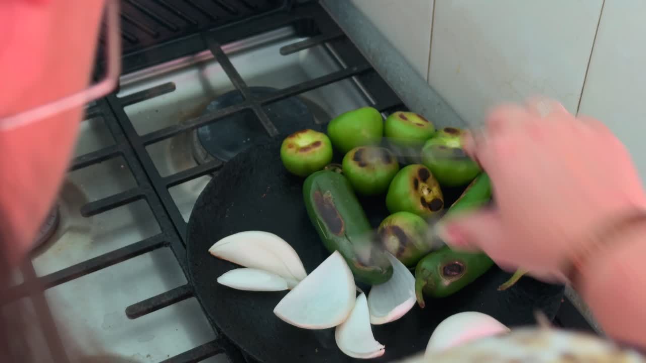 Woman’s hand grilling tomatillos, zucchini, and onions on stovetop comal, close up