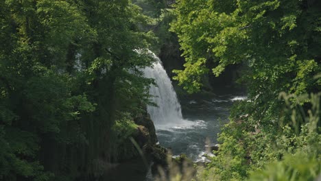 Lush-green-foliage-framing-a-majestic-waterfall-flowing-into-a-serene-river-in-Rastoke,-Croatia