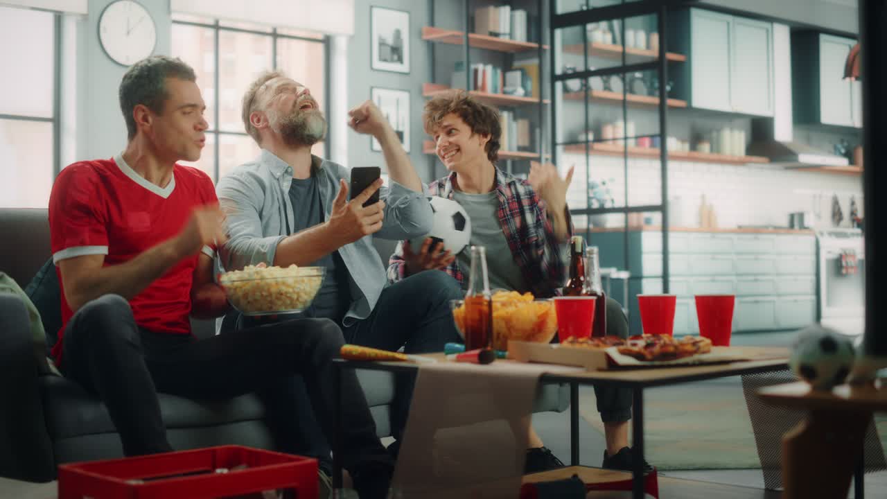 집에서 세 명의 축구 팬이 소파에 앉아 tv에서 스포츠 경기를보고, 스마트폰 앱을 사용하여 온라인 베팅을하고, 팀이 챔피언십에서 우승했을 때 축하하고, 친구들이 환호하고, 간식을 먹고, 좋아하는 축구 클럽 경기를 시청합니다.
