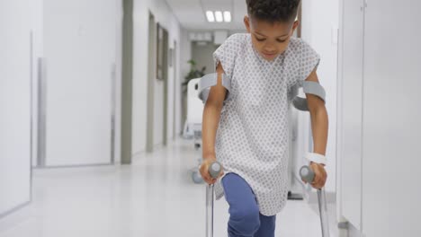 african american male doctor walking with child patient using crutches at hospital