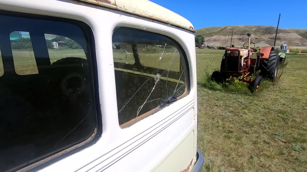 Broken window in a old rusty white truck sitting in a field next to a old red tractor on a farm