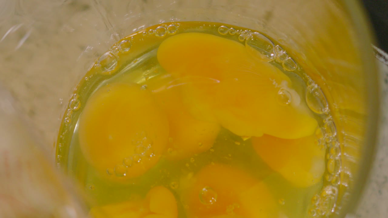 Overhead View of Raw Eggs Being Poured in Slow Motion into Measuring Jug with Multiple Eggs Ready to Make Scrambled Eggs for High Protein Breakfast.