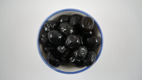 bowl filled with black olives slowly rotates on white background