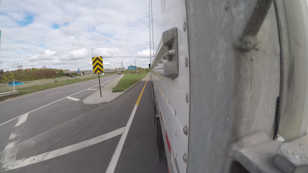 POV shot from the back left of a semi truck trailer driving on the freeway, taking an exit ramp on a cloudy day