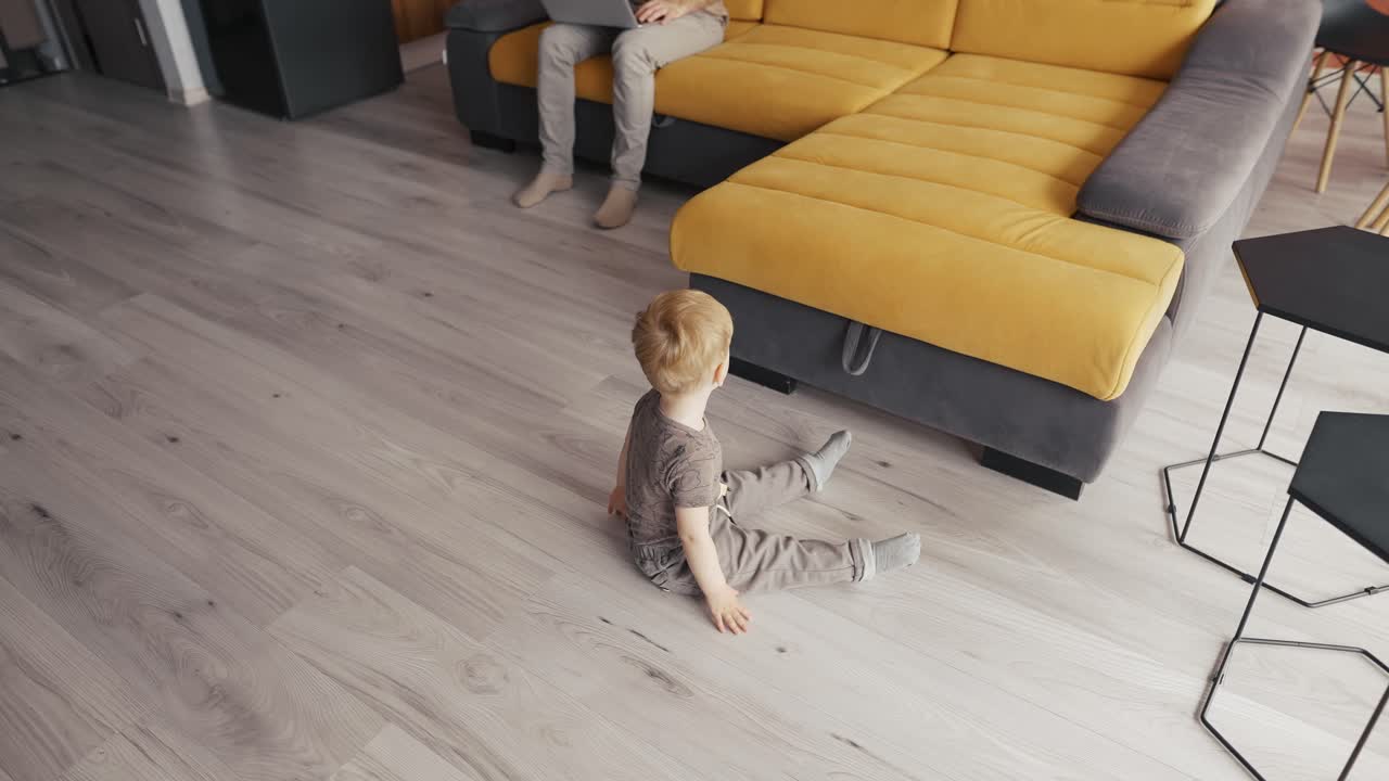 pequeño hijo pequeño divirtiéndose en casa mientras su padre está ocupado con la computadora portátil en el sofá