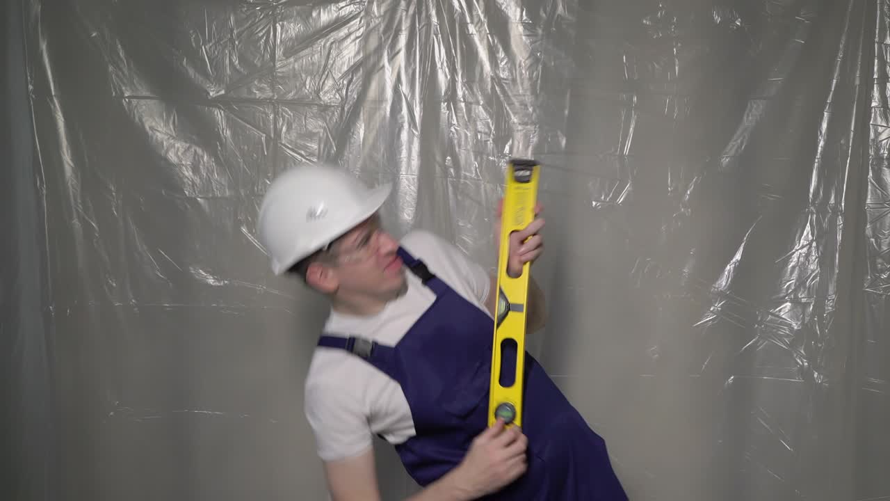 파란색 오버롤과 색 하드 모자를 입은 건축가. 기타처럼 재는, 춤추는