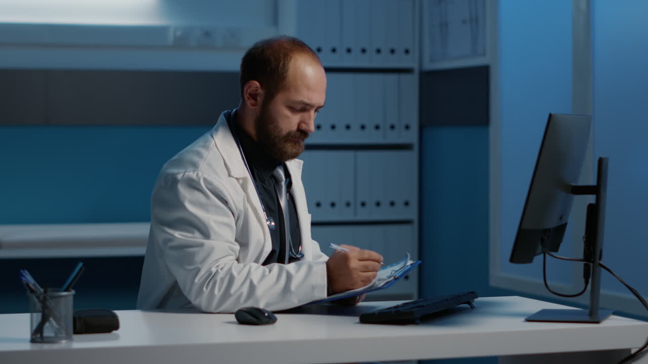 Doctor working at desk with computer and clipboard