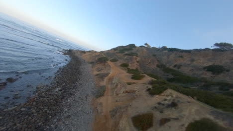 volando a lo largo de un acantilado con vista al océano en un dron de carreras con vista en primera persona