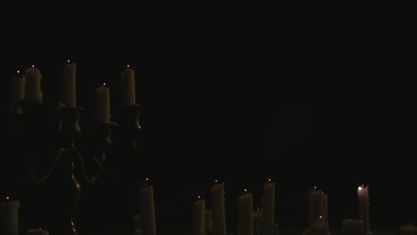 a group of white candles some on a candelabra lit up then blown out by the wind in slow motion