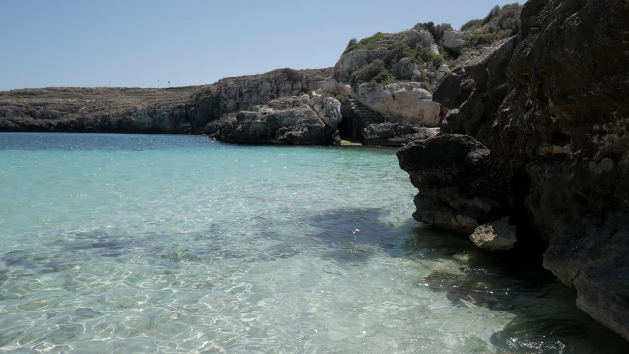 Clear turquoise waters in Cala Binidali, Menorca with rocky shoreline
