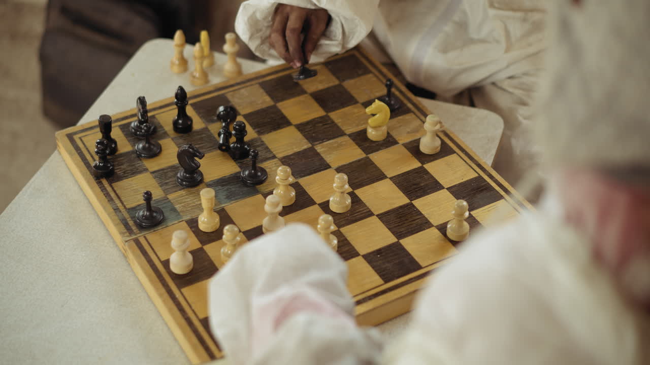 Close up of focused hand in white sleeve moving black piece on rustic chessboard during game with wooden chess pieces, strategy and tension are evident as players make thoughtful decisions