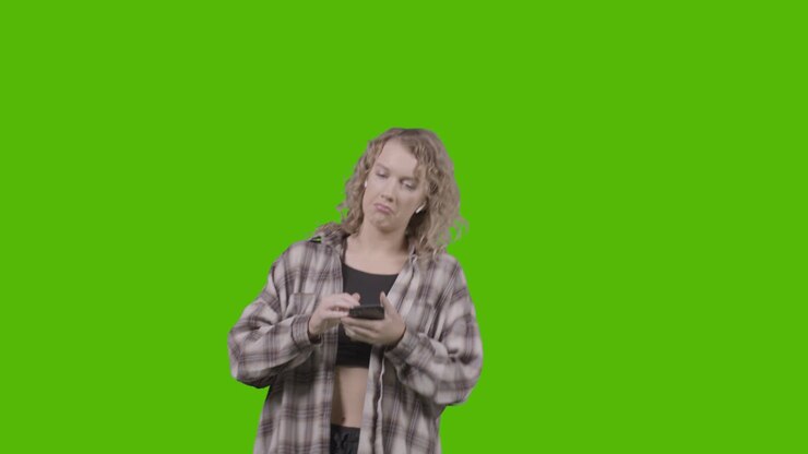 Scatto in studio di giovane donna che ascolta musica al cellulare e balla su green screen 1.