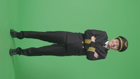 녹색 스크린 배경 스튜디오에 서있는 동안 미소 짓고 카메라에 팔을 는 아시아 남자 조종사