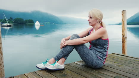 A-Woman-Sits-On-A-Wooden-Pier-Looks-At-The-Mountains-And-Mountain-Lake-In-Austria
