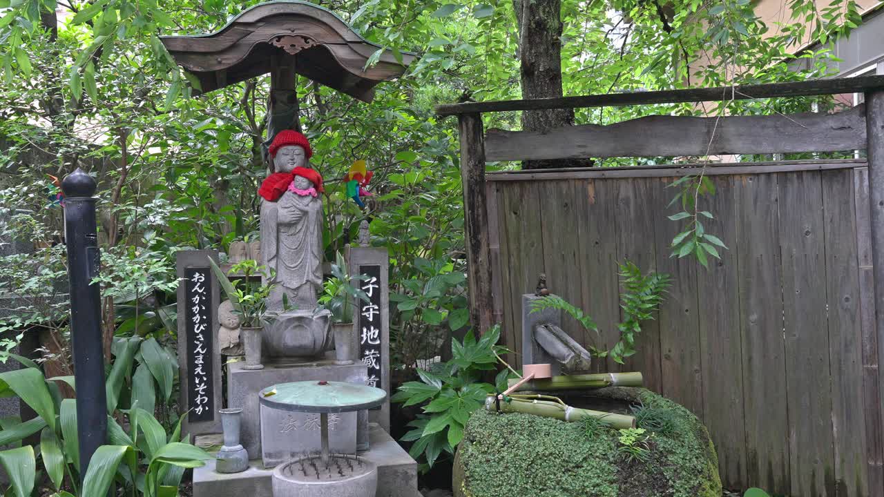 A serene Jizo statue adorned with a red hat stands next to a traditional Japanese garden water basin (tsukubai) and bamboo accents.