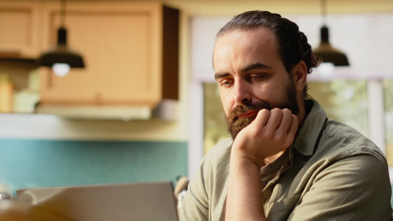 Primer plano de un hombre comiendo croissants y usando un portátil en la mesa de la cocina