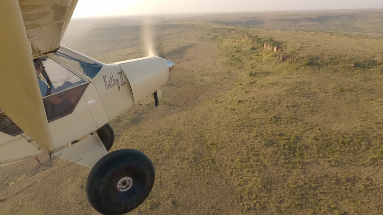 Avião sobre a savana com vista aérea de uma falésia rochosa distante.