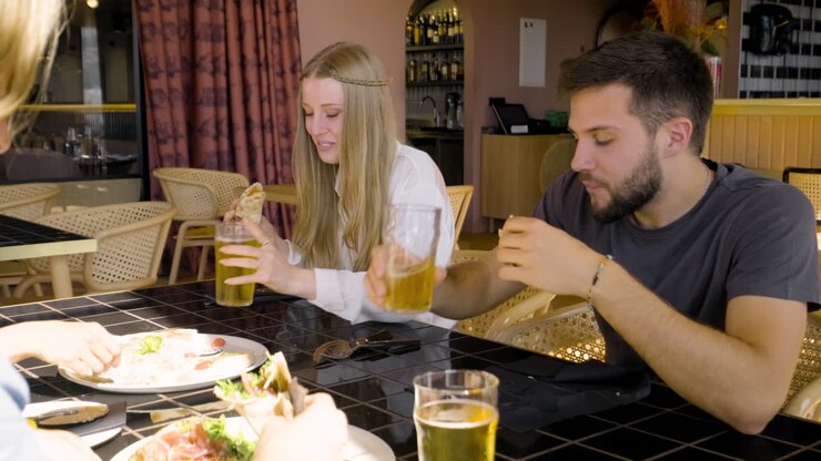 Primo piano di una donna e un uomo che parlano e mangiano pizza con i loro amici al tavolo di un ristorante 2