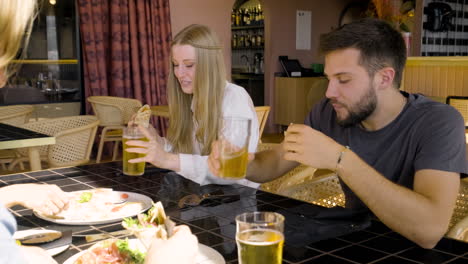 close up view of a woman and man talking and eating pizza with their friends at restaurant table 2