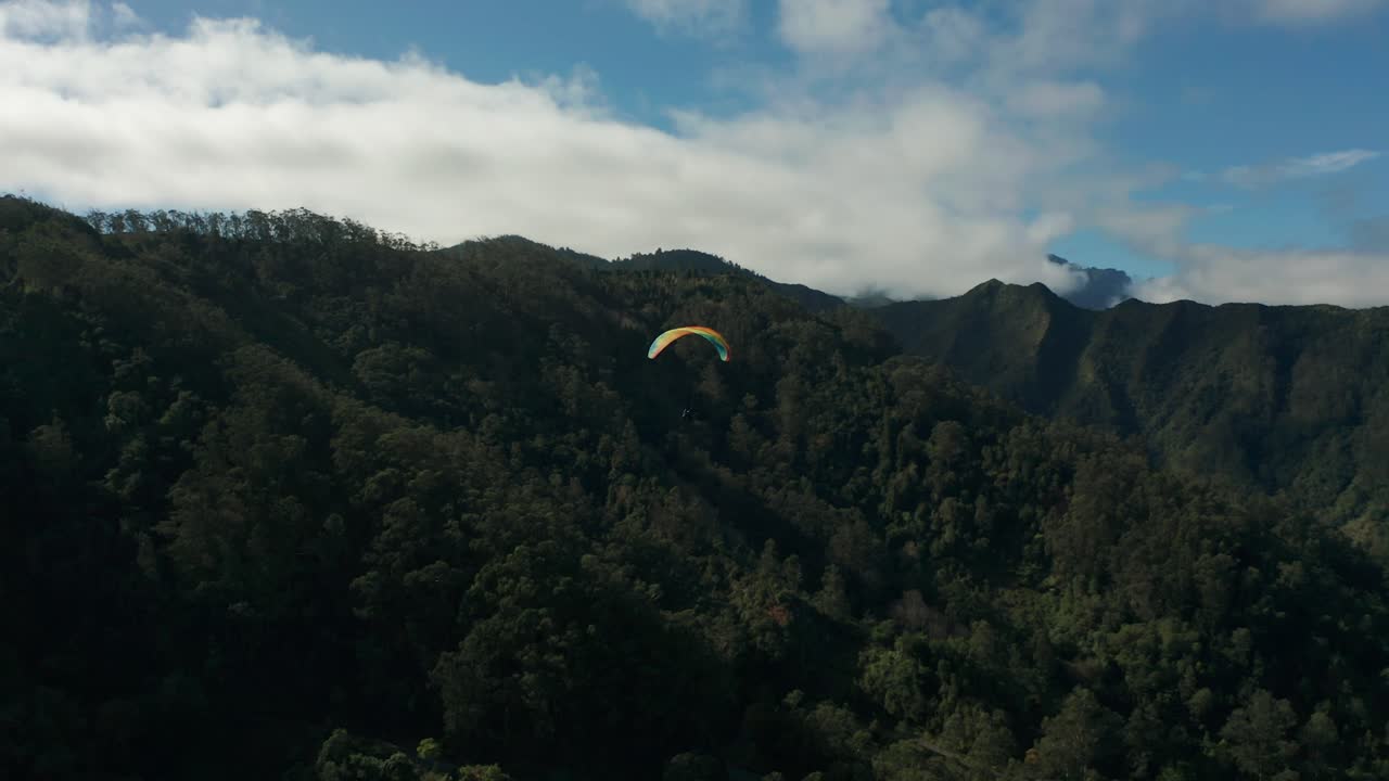 Vue aérienne d'un parapentiste planant dans les airs au-dessus des montagnes luxuriantes et boisées de l'île de Madère