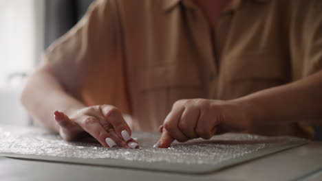 woman presses fingers on bubble wrap sitting at table