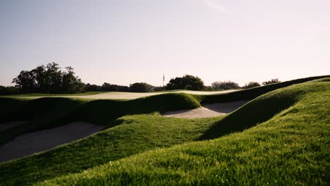 push in shot towards the green of a golf hole during sunrise showing the flag and green side bunkers