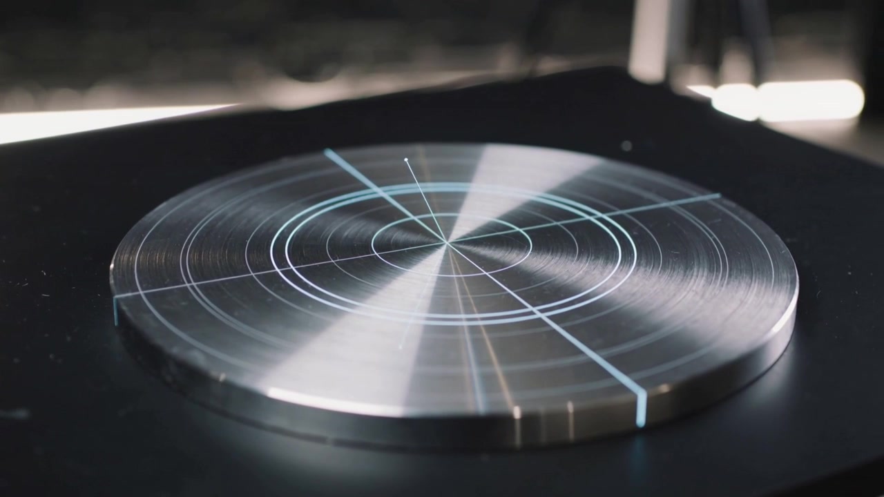 Sweeping light moving bright wedge across metal platter on studio bench, revealing concentric rings