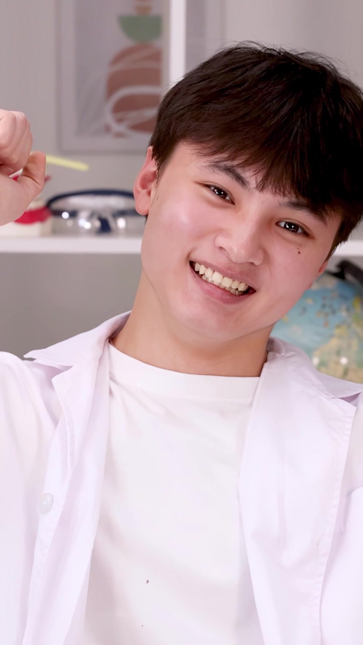 A smiling student in a white lab coat raises his fist in a science classroom.