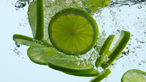 agua suculenta de cal cae sobre un fondo blanco. cítricos flotando bajo el agua de cerca.