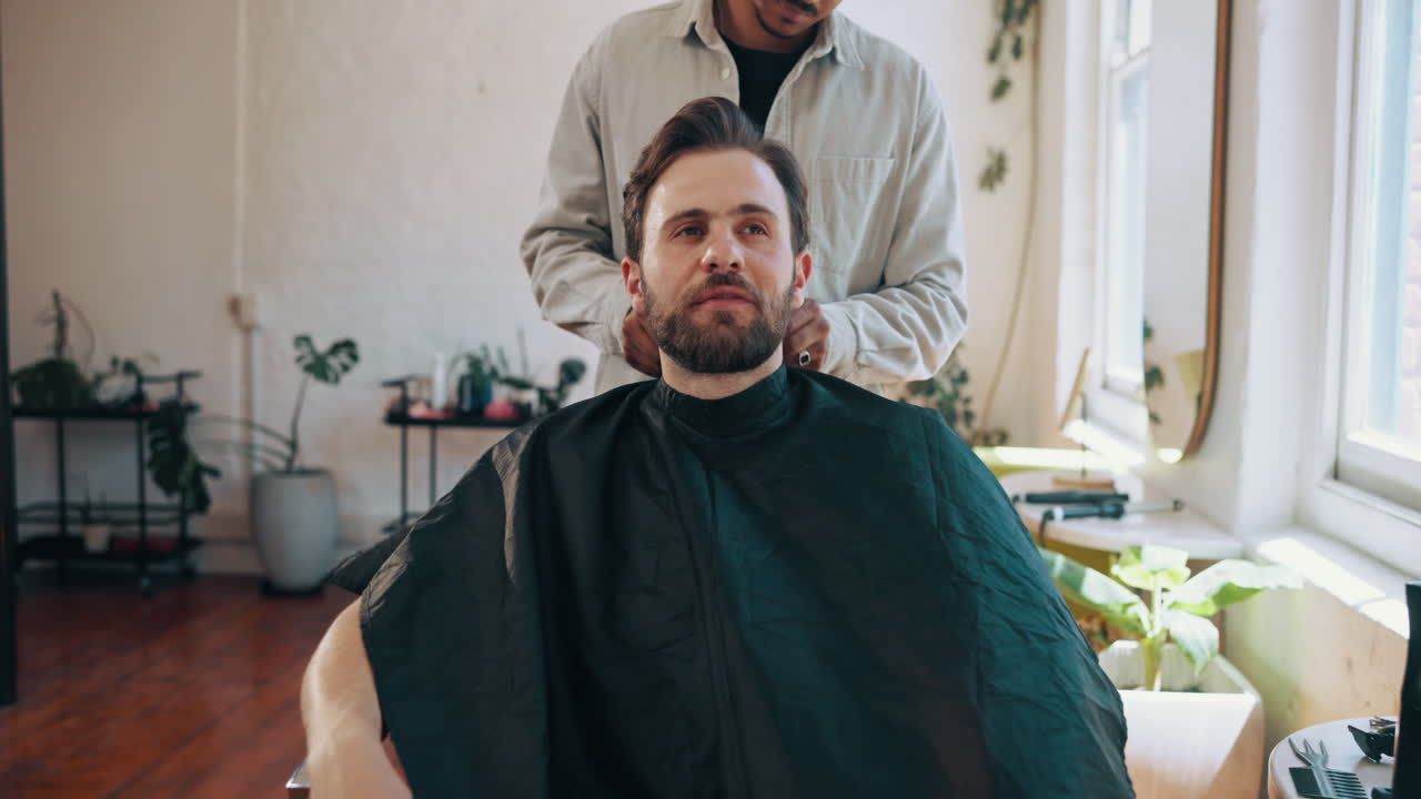 Frisør sætter beskyttelseskappe på smilende mandlig kunde i salonen.