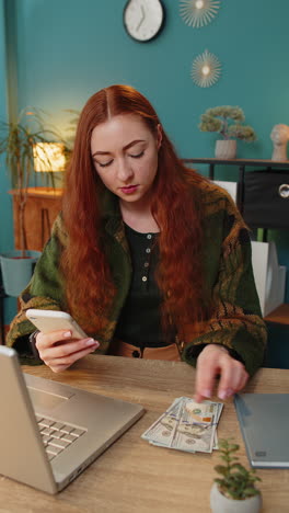 Una-Mujer-Feliz-Y-Sonriente-Contando-Dinero-En-Efectivo-En-Dólares-Usando-Ingresos-Por-Teléfono-Inteligente-Ahorra-La-Lotería-En-Casa