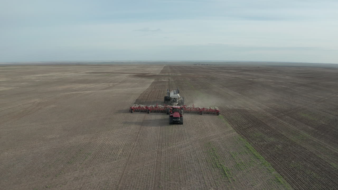 un tractor sembrador sembrando en las tierras de cultivo en corriente rápida, saskatchewan, canadá - disparo de dron ascendente