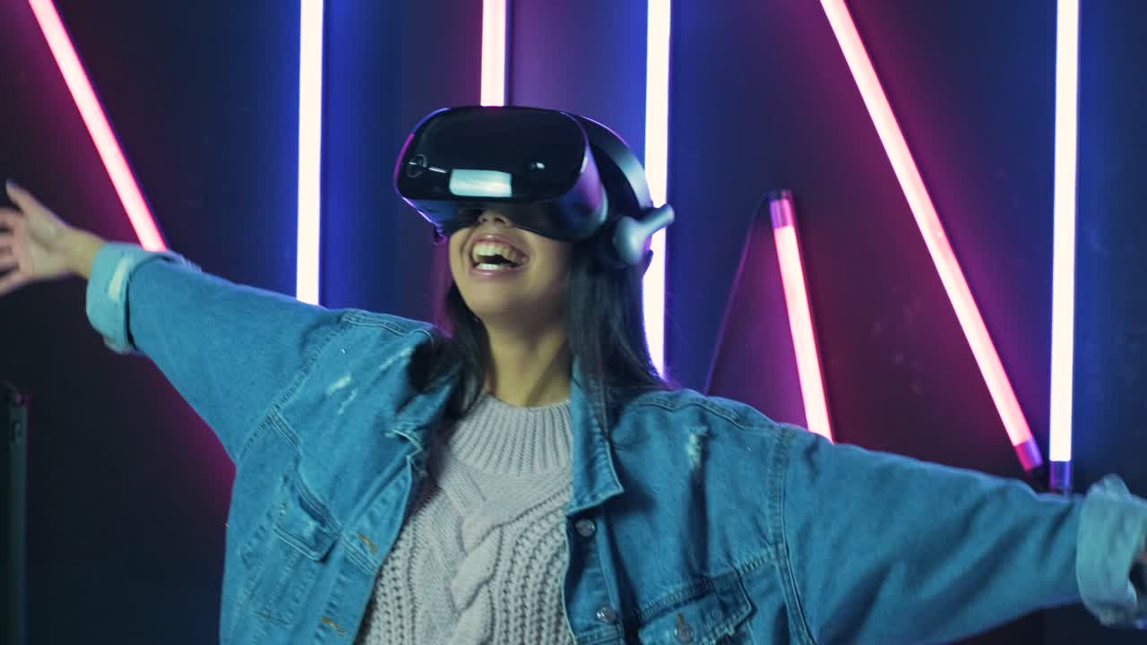 giovane donna felice che gioca, balla e sorride nell'auricolare vr. casco di realtà virtuale sullo sfondo di illuminazione a colori